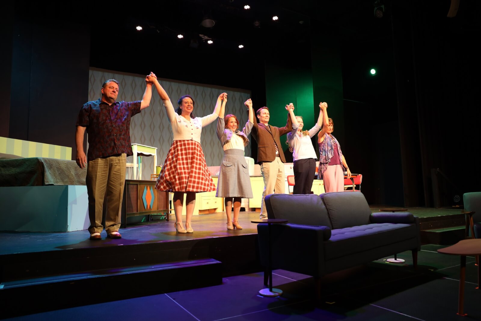 Raven Performing Arts Theater A group of six people joyfully raise their hands together on a stage with a retro set design in Healdsburg, California.