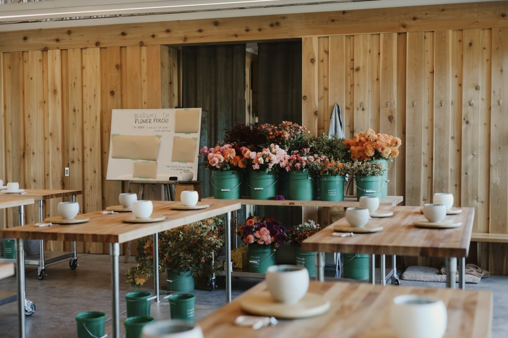 A bright, airy room with wooden walls and floors, filled with tables set with white cups and saucers, surrounded by vibrant flower arrangements in green buckets in Healdsburg, California.