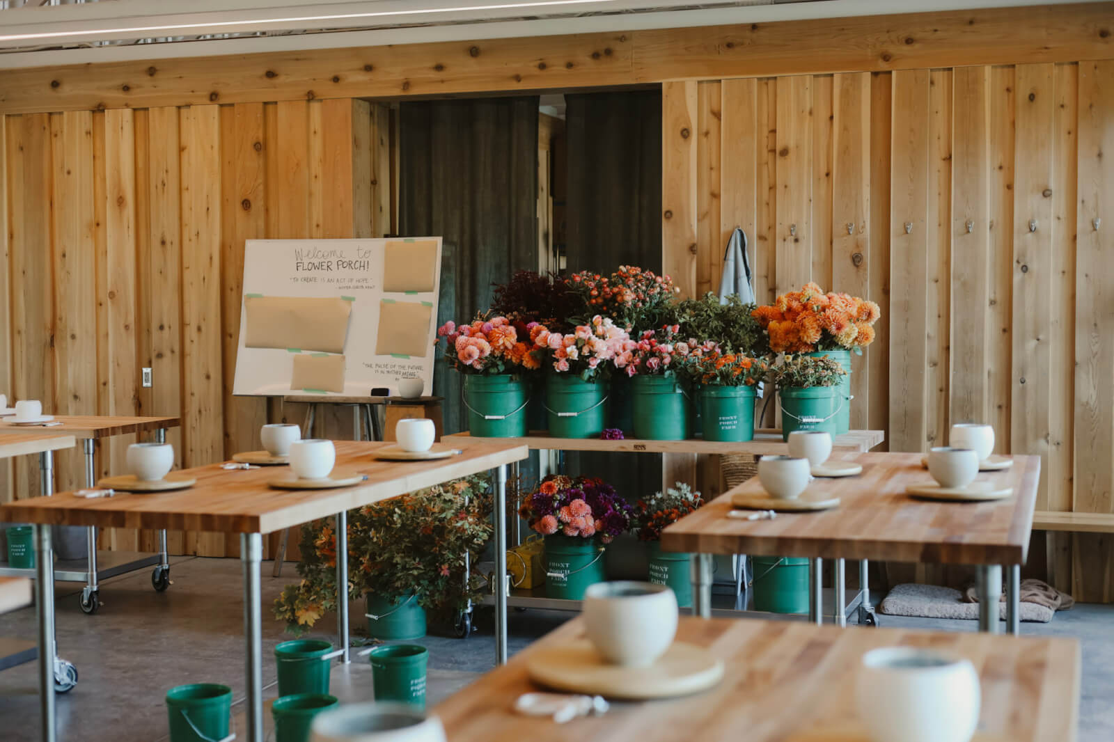 A bright, airy room with wooden walls and floors, filled with tables set with white cups and saucers, surrounded by vibrant flower arrangements in green buckets in Healdsburg, California.