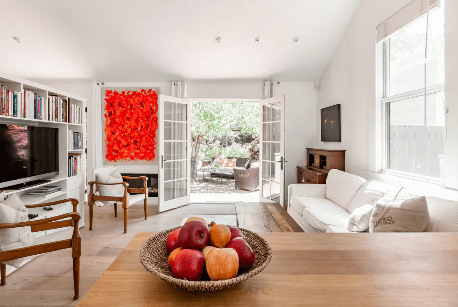 Healdsburg Contemporary Cottage A bright, airy living room with white walls, wooden floors, and a basket of apples on the coffee table in Healdsburg, California.