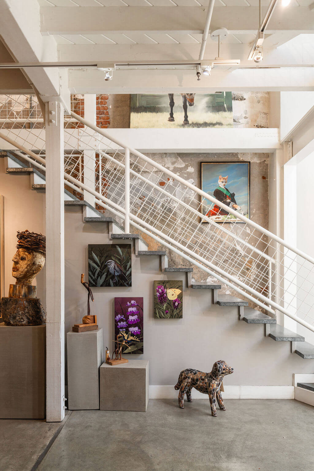 NOMAD District A modern staircase with a white railing leads up to a gallery wall featuring various artworks in Healdsburg, California.