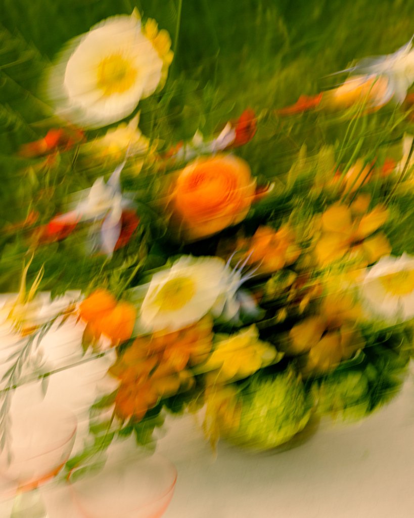 A vibrant, blurred bouquet of colorful flowers, including white, yellow, orange, and red blooms, set against a green background in Healdsburg, California.