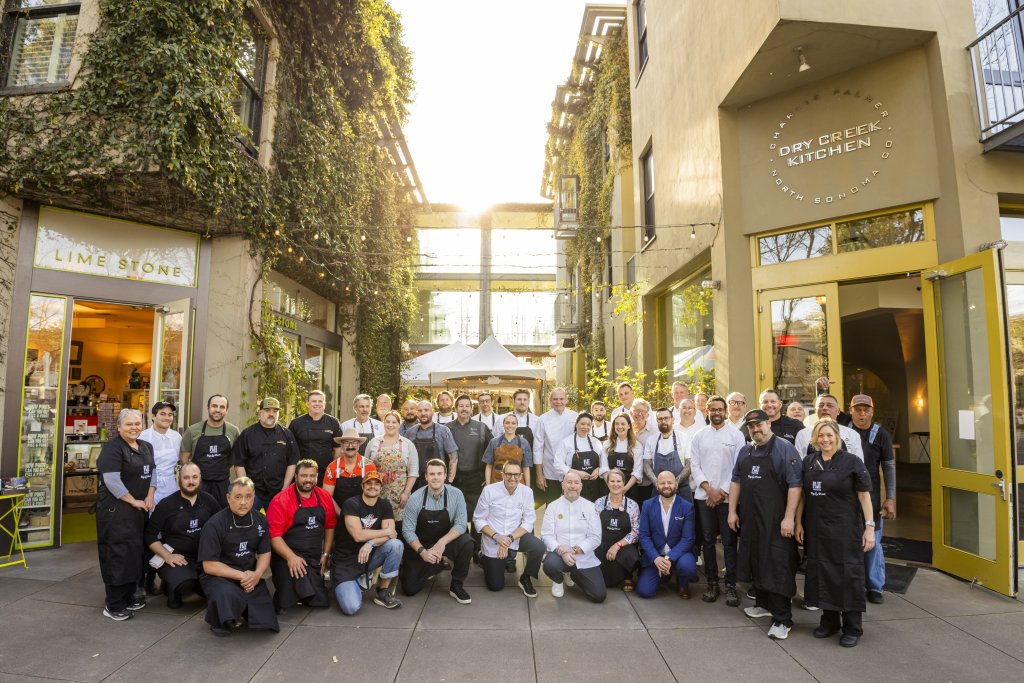 A large group of chefs and kitchen staff from Dry Creek Kitchen and Lime Stone restaurant pose together outside in a lush, ivy-covered courtyard in Healdsburg, California.