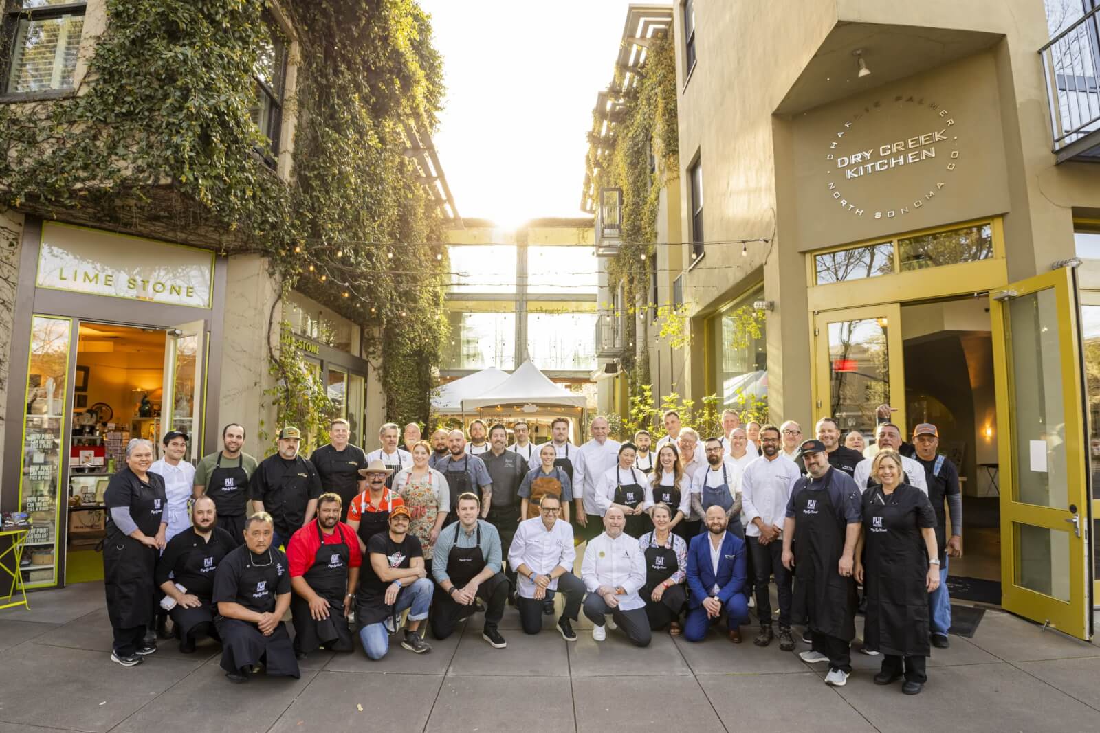 A large group of chefs and kitchen staff from Dry Creek Kitchen and Lime Stone restaurant pose together outside in a lush, ivy-covered courtyard in Healdsburg, California.