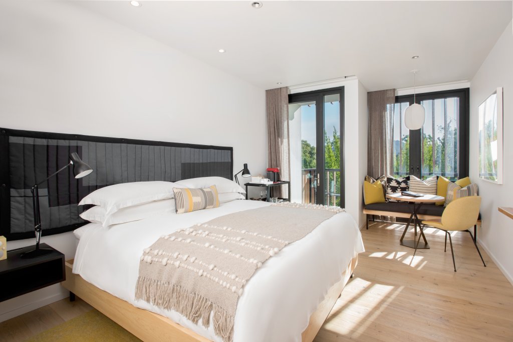 A modern bedroom with a large bed, a cozy seating area, and floor-to-ceiling windows overlooking a serene outdoor view in Healdsburg, California.