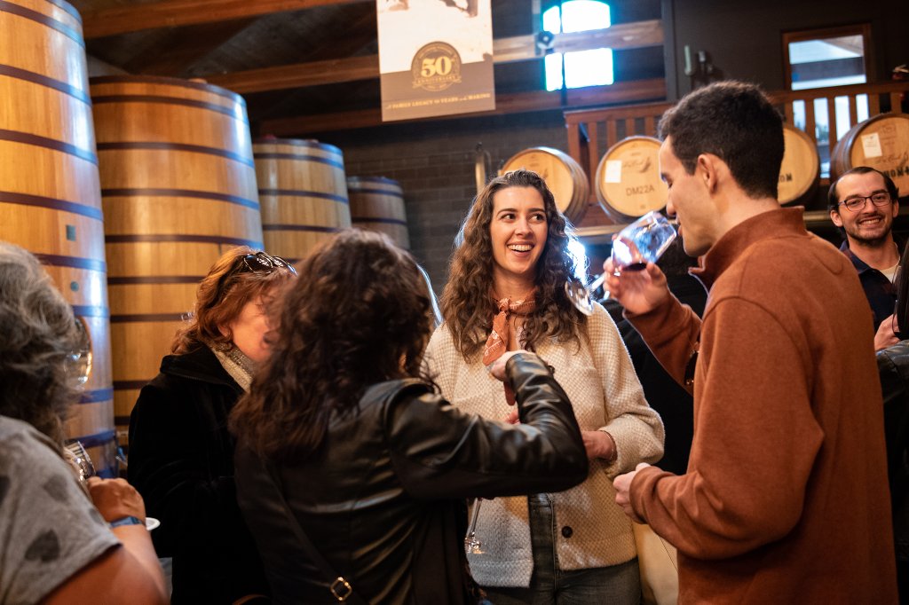 A group of people are gathered in a cozy wine cellar, surrounded by large wooden barrels, enjoying wine and lively conversation in Healdsburg, California.