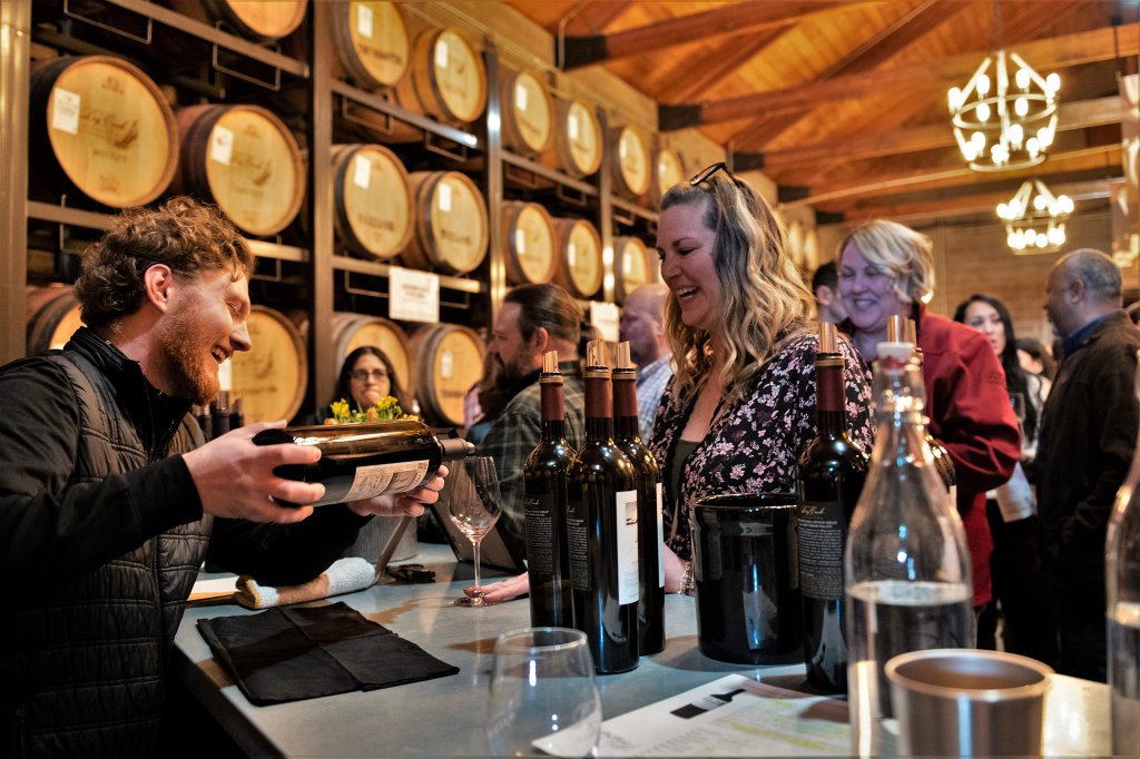 A lively wine tasting event in a cozy cellar with wooden barrels and chandeliers, where guests sample various wines and enjoy each other's company in Healdsburg, California.