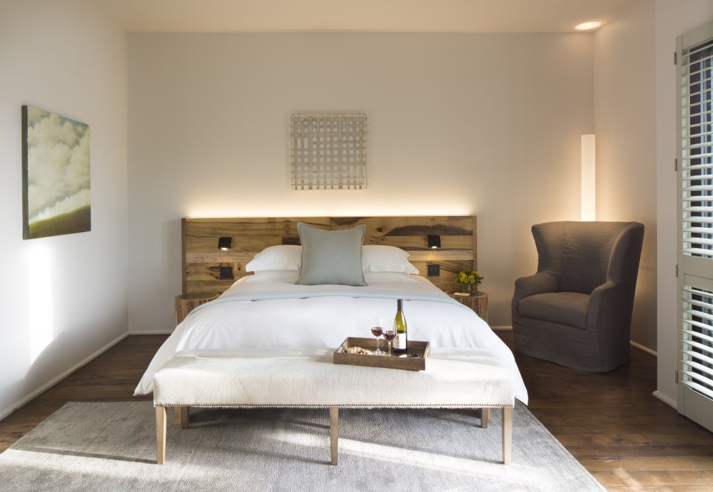 A serene bedroom with a wooden bed frame, white bedding, and a tray of wine glasses on the foot of the bed in Healdsburg, California.