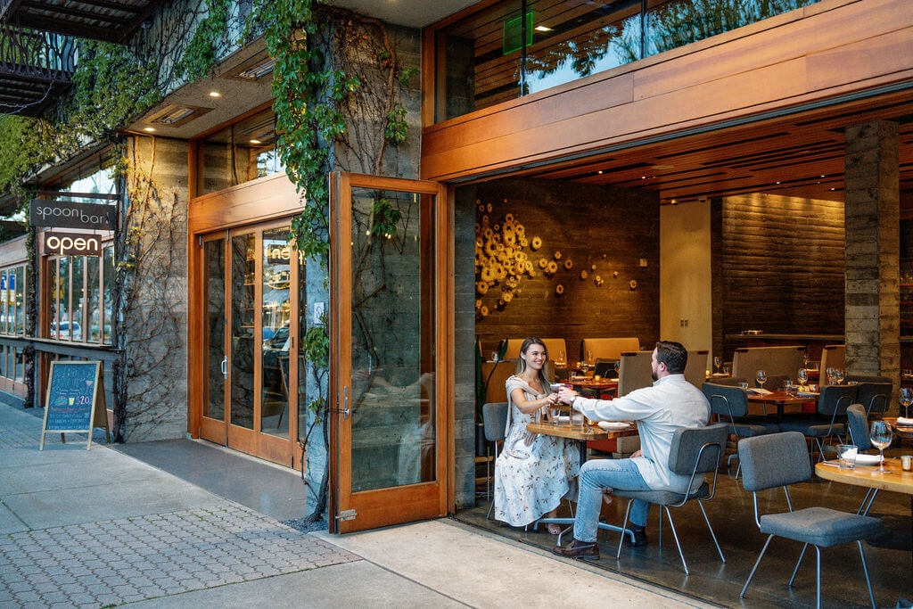 A couple enjoys a romantic dinner at an open-air restaurant with a lush green wall and modern decor in Healdsburg, California.