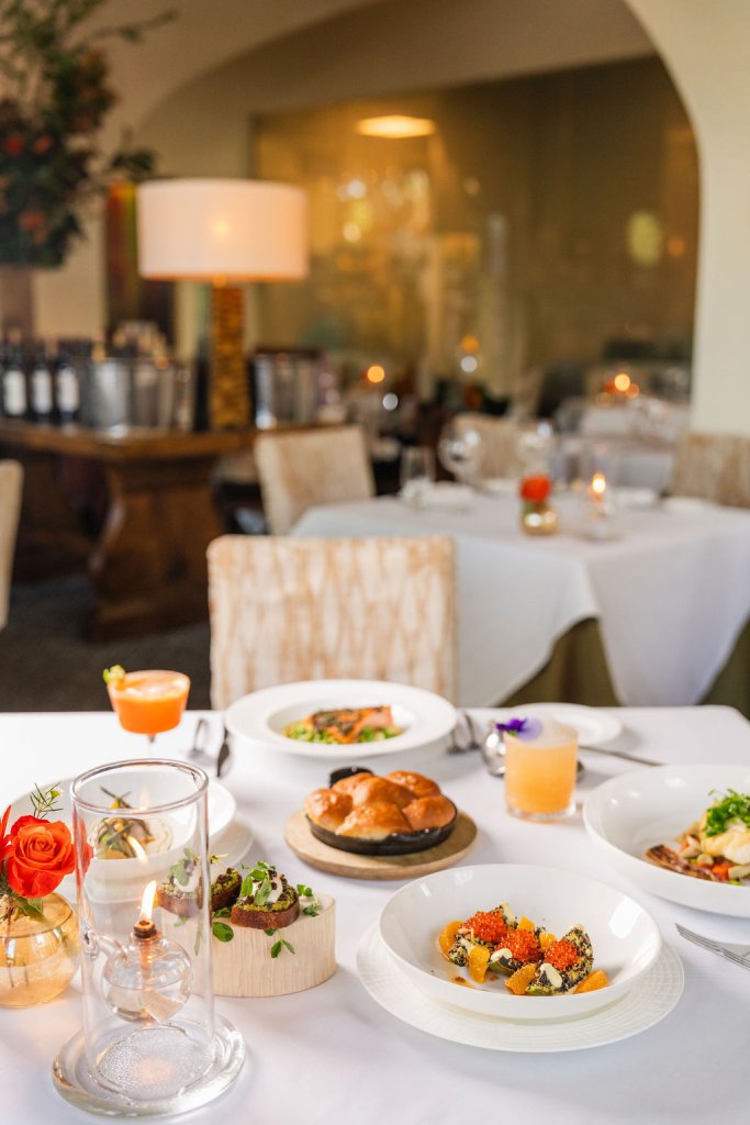 Elegant table setting with a variety of dishes, including a glass dome with a lit candle, colorful cocktails, and a plate of caviar-topped avocado slices in Healdsburg, California.