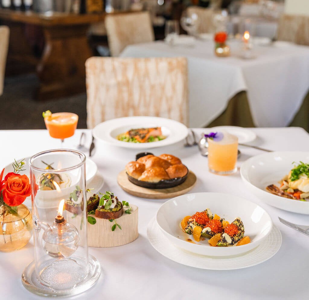 Celebrate Sonoma Gourmet Getaway Elegant table setting with a variety of dishes, including a glass dome with a lit candle, colorful cocktails, and a plate of caviar-topped avocado slices in Healdsburg, California.