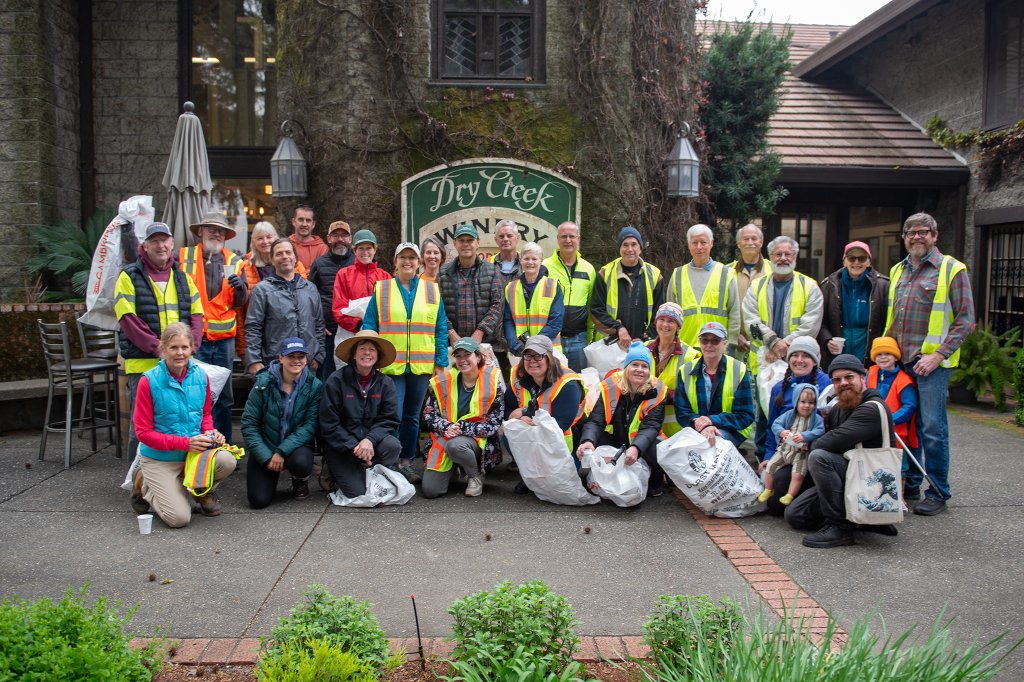 A group of volunteers wearing high-visibility vests and holding trash bags pose for a photo after a community clean-up event at Dry Creek Winery in Healdsburg, California.