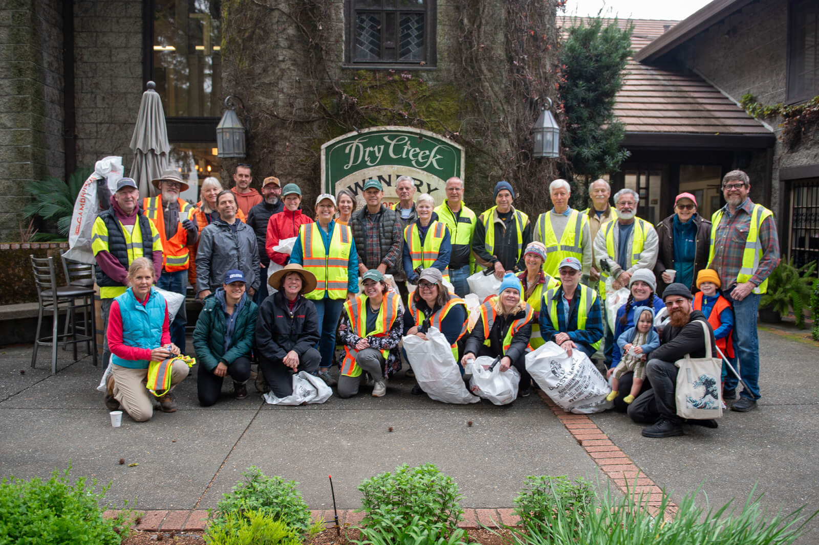 A group of volunteers wearing high-visibility vests and holding trash bags pose for a photo after a community clean-up event at Dry Creek Winery in Healdsburg, California.