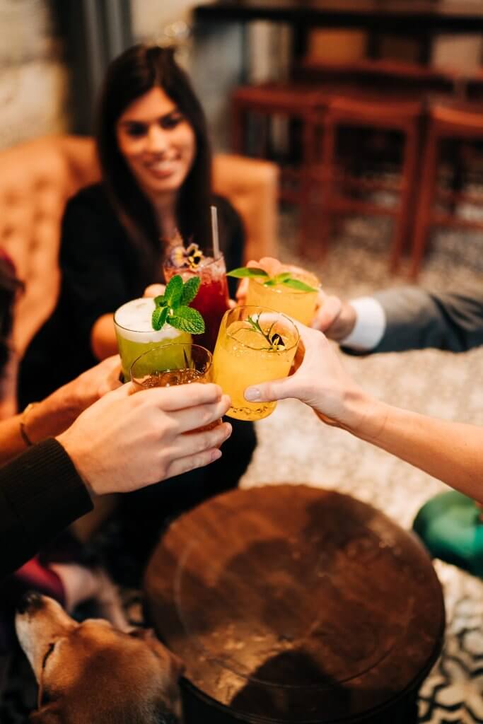 A group of friends is toasting with colorful cocktails in a cozy bar setting in Healdsburg, California.
