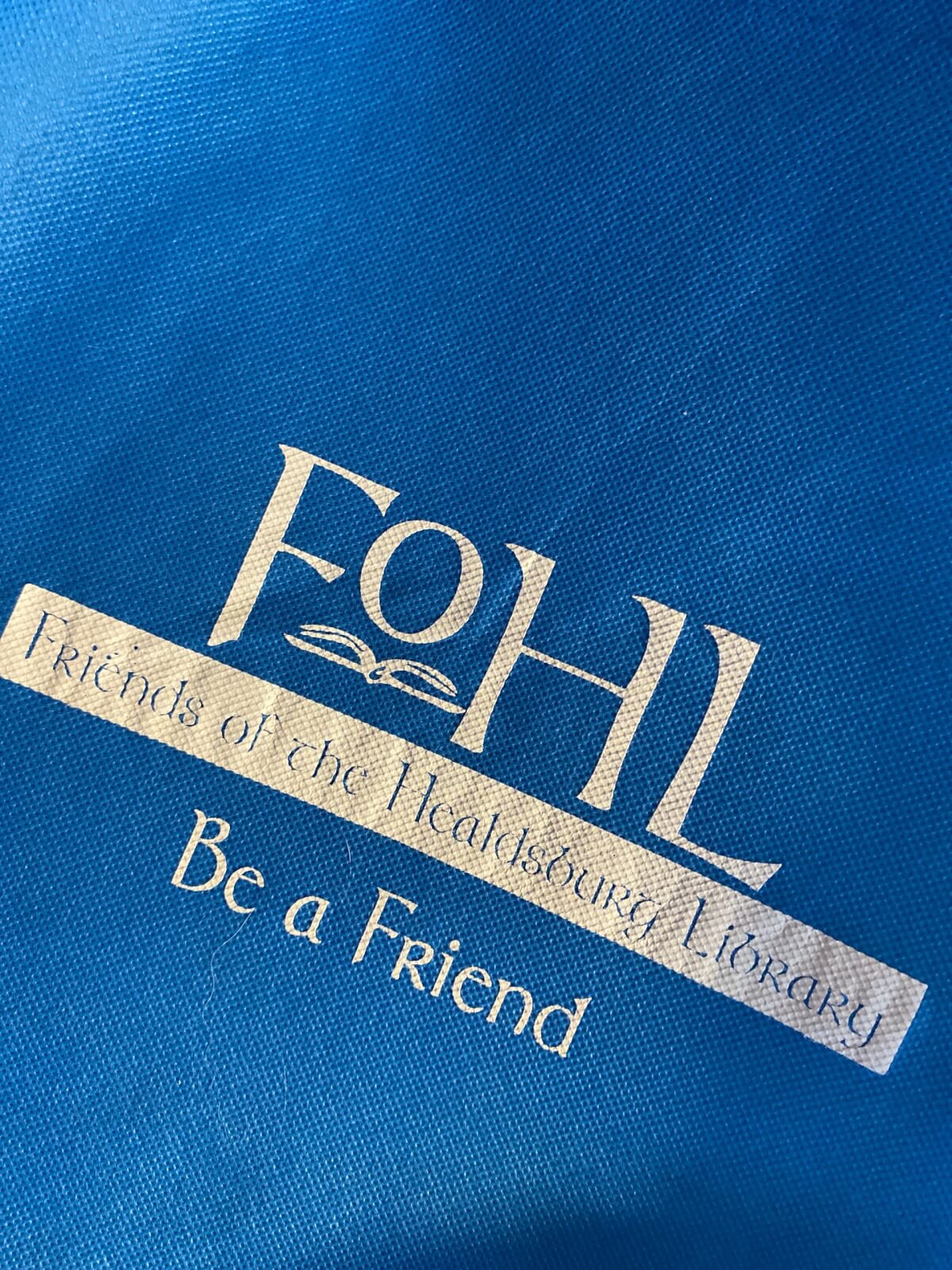A blue tote bag with the logo and slogan of the Friends of the Healdsburg Library in Healdsburg, California.