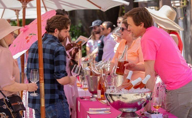 A lively outdoor gathering with people enjoying wine and conversation under colorful umbrellas in Healdsburg, California.