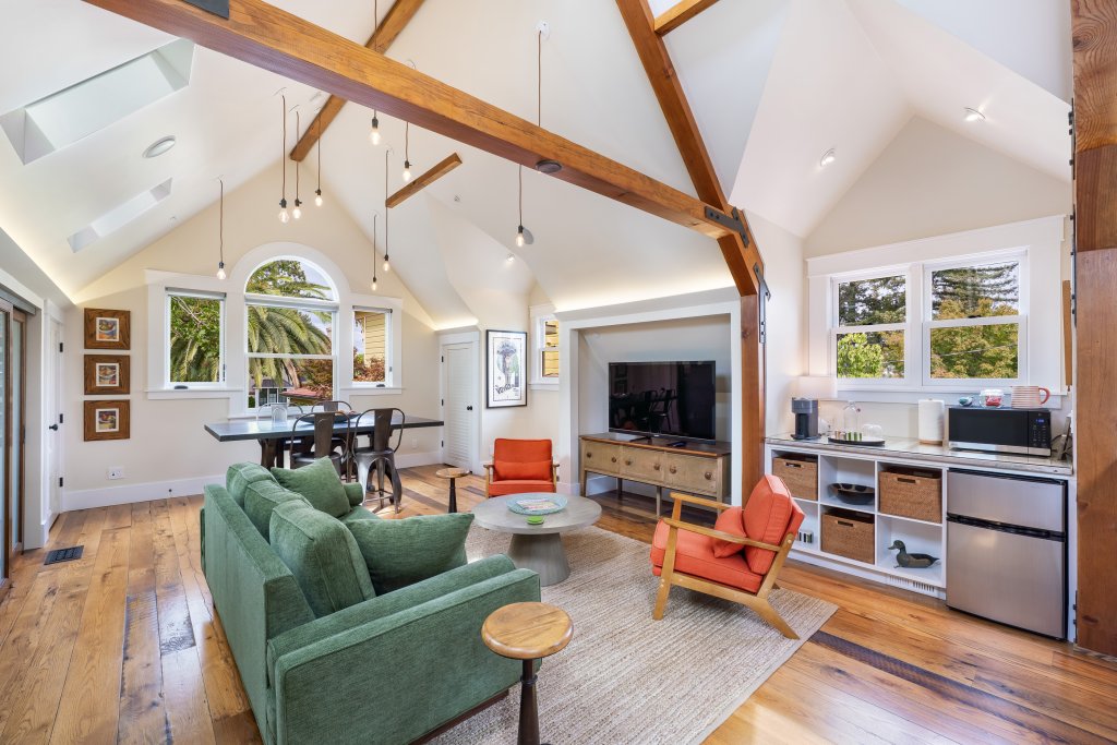 A cozy, modern living room with a green sofa, orange chairs, and a dining area featuring a wooden table and chairs in Healdsburg, California.