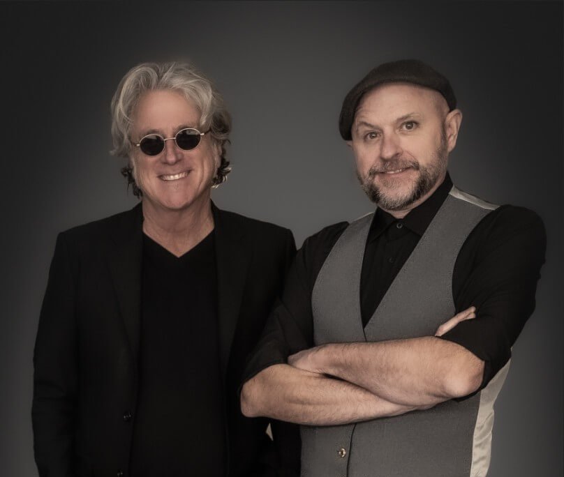 Two men dressed in black and gray attire stand confidently with arms crossed against a dark background in Healdsburg, California.