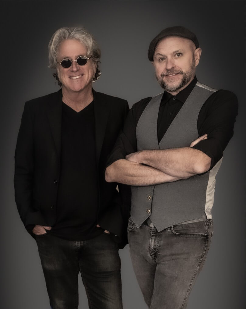 Two men dressed in black and gray attire stand confidently with arms crossed against a dark background in Healdsburg, California.