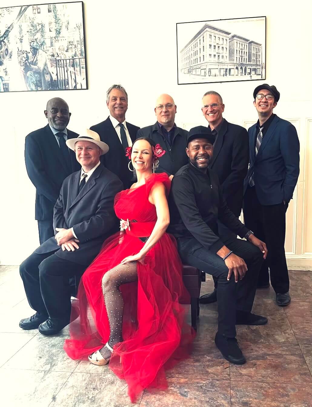A group of eight elegantly dressed individuals, including a woman in a striking red gown, pose together in a formal setting with framed artwork on the walls in Healdsburg, California.