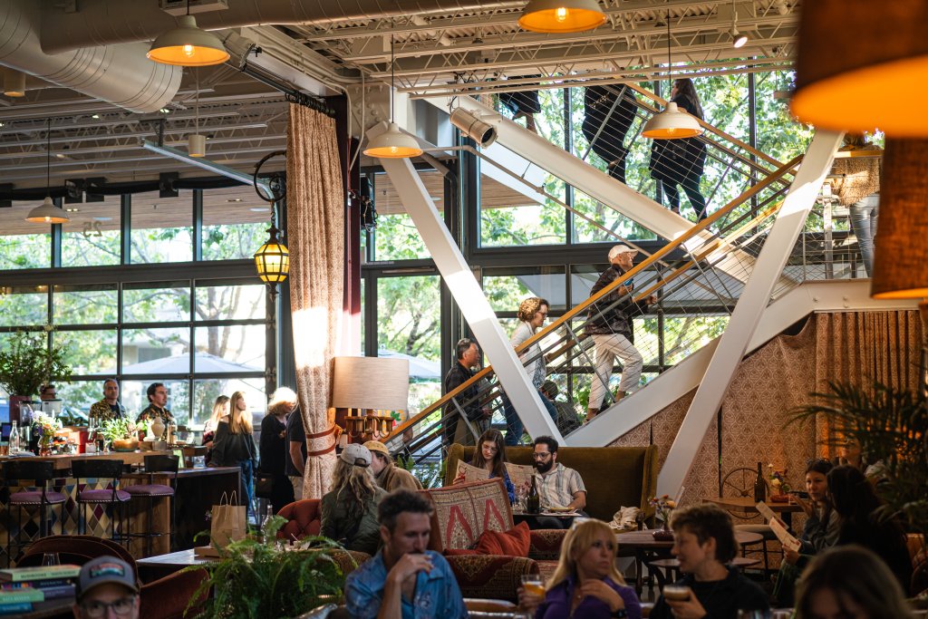A bustling indoor-outdoor restaurant with a modern design, featuring a staircase, large windows, and a variety of seating areas in Healdsburg, California.