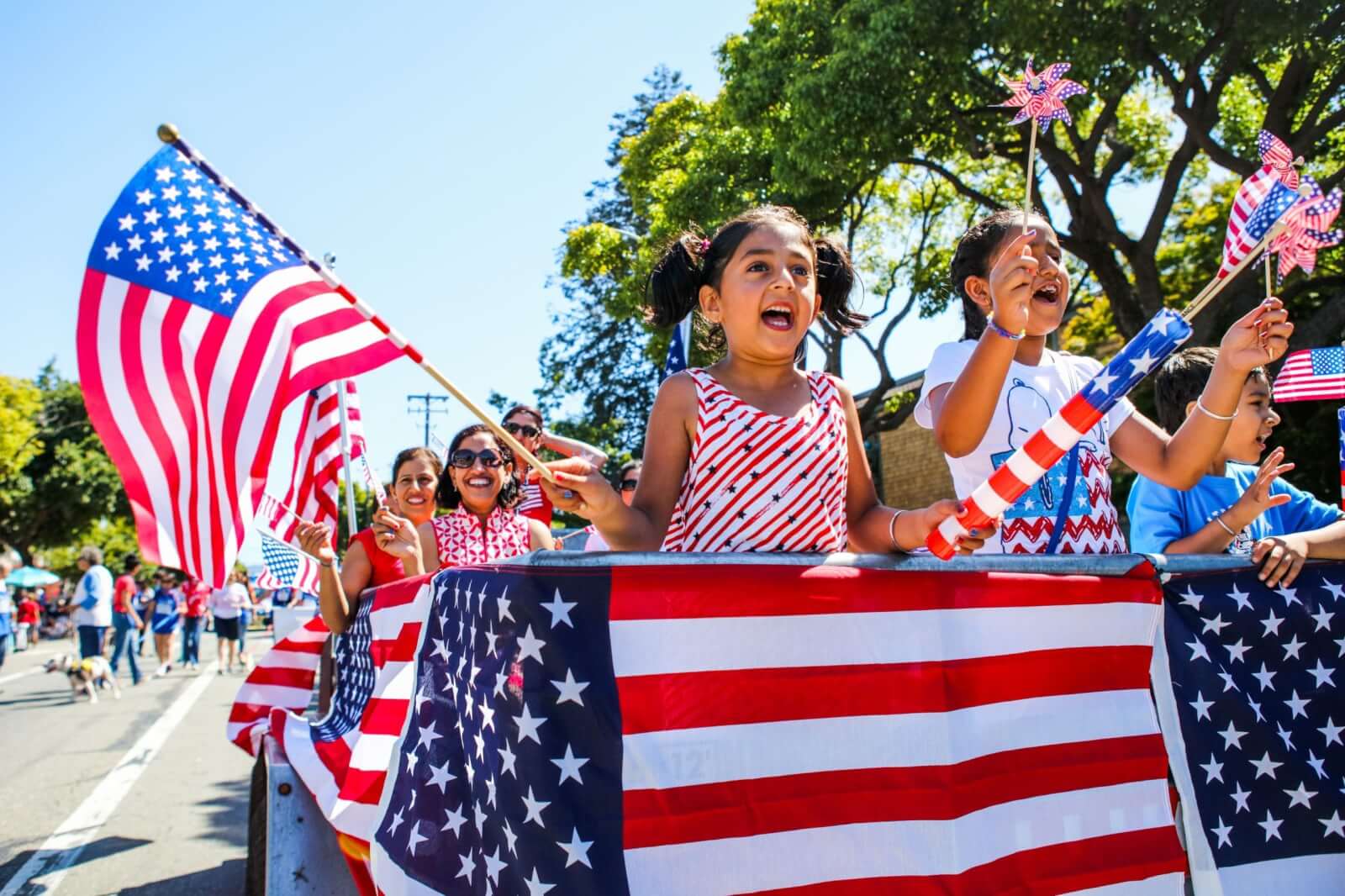 A vibrant Fourth of July parade float adorned with American flags, featuring enthusiastic children waving flags and holding patriotic pinwheels, with a backdrop of cheering spectators and a clear blue sky in Healdsburg, California.