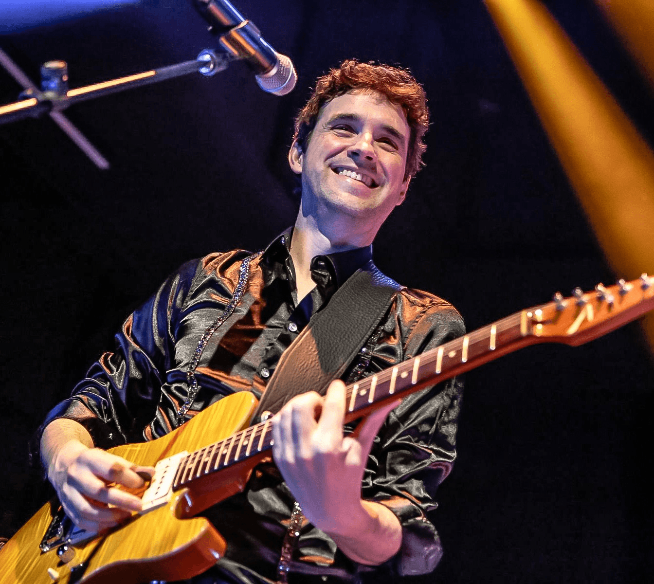 A smiling musician playing an electric guitar on stage under stage lights in Healdsburg, California.